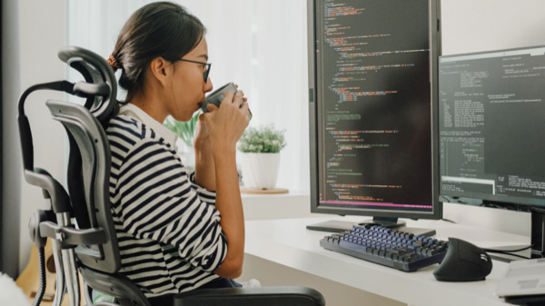 Entwickler trinken Kaffee beim Überprüfen von Code auf dualen Monitoren.